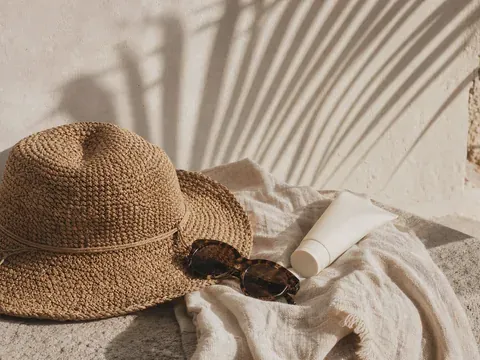 A straw sun hat, sunglasses and sunscreen on a linen towel in warm sunlight