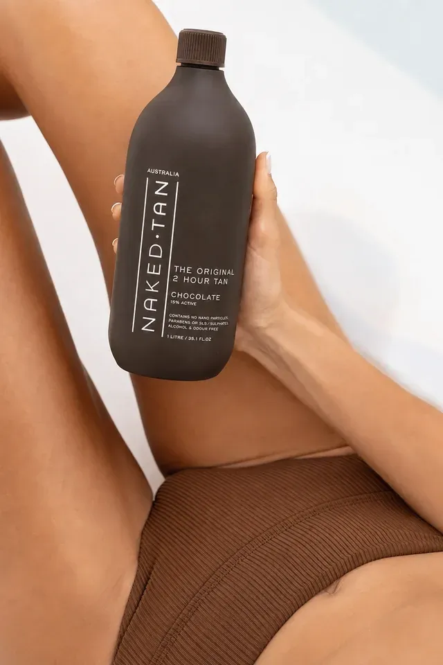 A woman holding a bottle of Naked Tan Chocolate spray tan solution