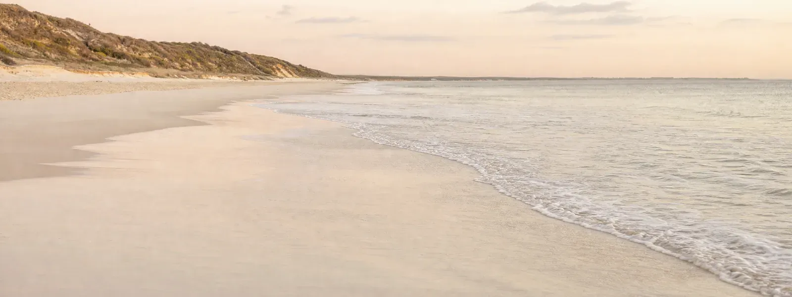 A wide, empty white-sand beach in soft morning light