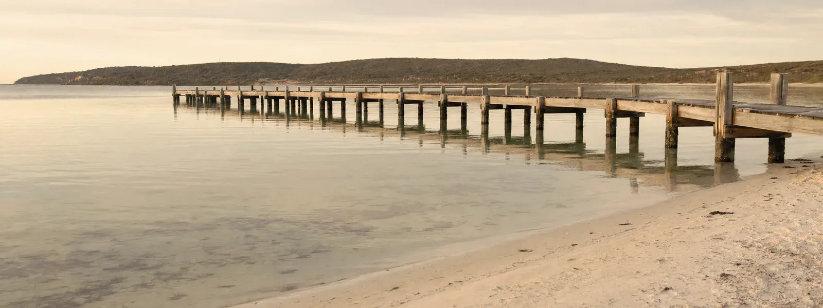 A calm sheltered bay with a long timber jetty in warm afternoon light